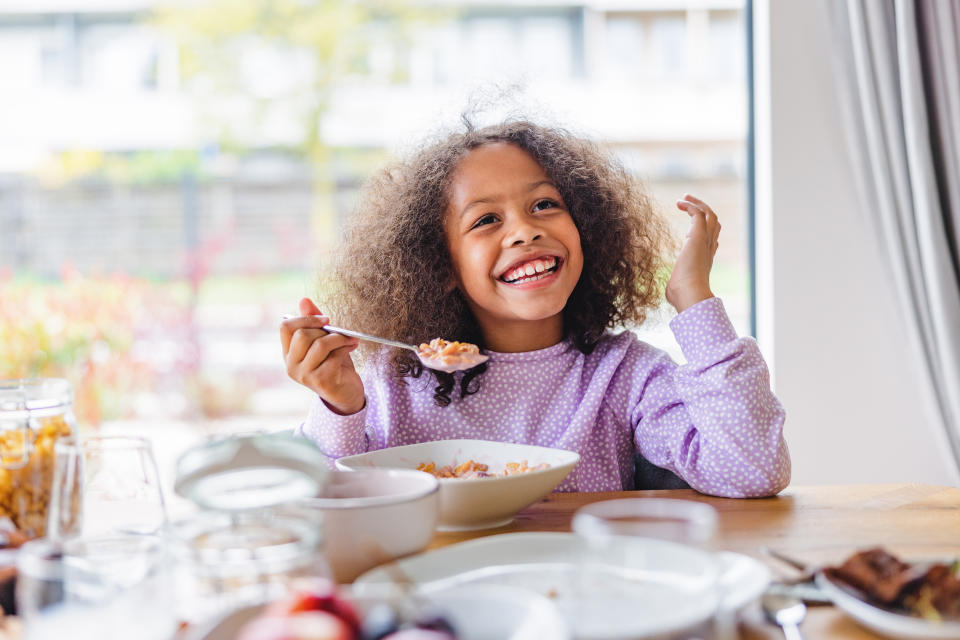 Child enjoying a bowl of cereal at a breakfast table, smiling and looking happy