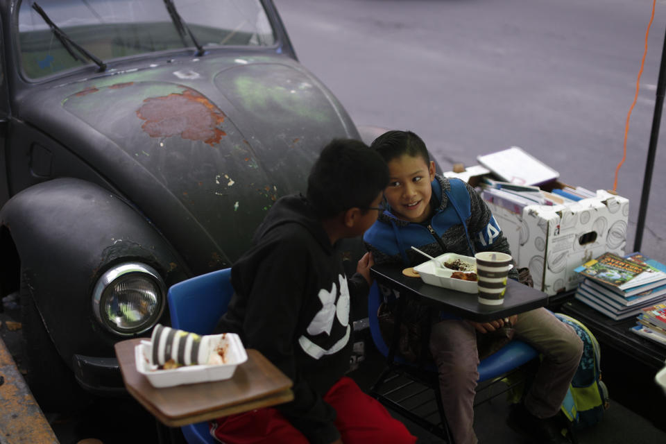 Brothers Bryan, right, and Emanuel Quintana, talk as they eat a donated breakfast prior to a history lesson in front of "Tortillerias La Abuela," or Grandma's Tortilla Shop, on the southern edge of Mexico City, Friday, Sept. 4, 2020. Concerned about the educational difficulties facing children during the coronavirus pandemic, the couple who run the tortilla shop adapted several spaces outside their locale to provide instruction and digital access to locale children who don't have internet or TV service at home, a project which has attracted donations and a waiting list of students. (AP Photo/Rebecca Blackwell)