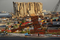 People pass next of a justice symbol monument that sits in front of towering grain silos gutted in the massive August 2020 explosion at the Beirut port that claimed the lives of more than 200 people, in Beirut, Lebanon, Wednesday, Aug. 4, 2021. A year after the deadly blast, families of the victims are consumed with winning justice for their loved ones and punishing Lebanon's political elite, blamed for causing the disaster through their corruption and neglect. (AP Photo/Hussein Malla)