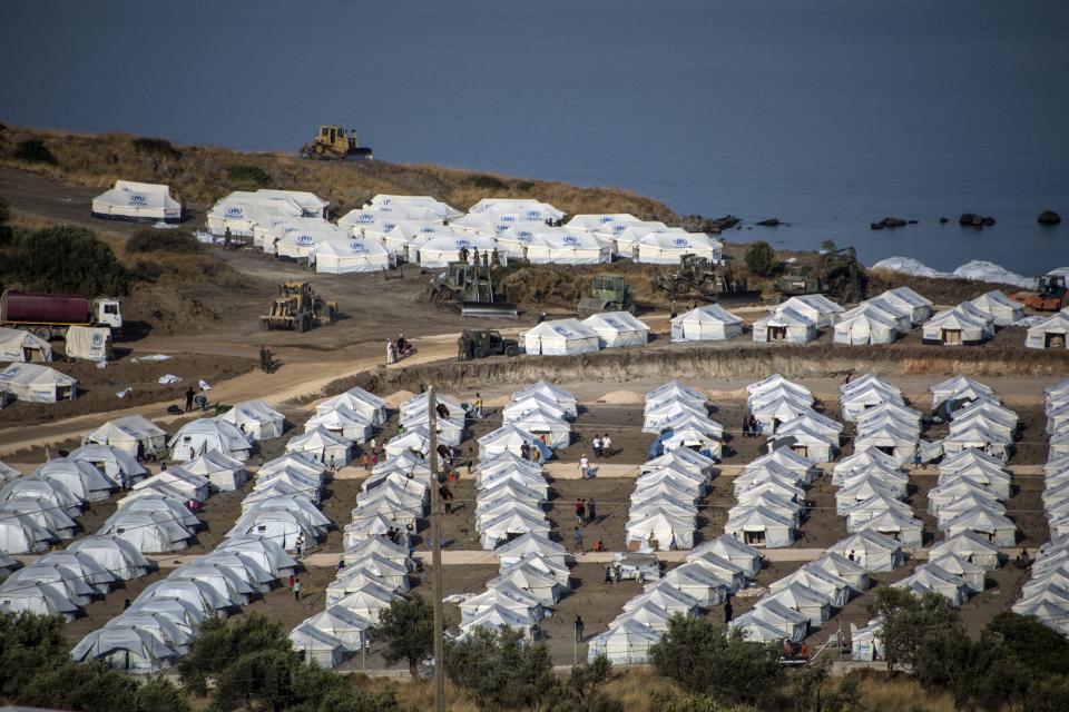 Heavy machines operate as migrants gather at the new temporary refugee camp in Kara Tepe, on the northeastern island of Lesbos, Greece, Thursday, Sept. 17, 2020. More than 5,000 asylum seekers left homeless after Greece's notoriously overcrowded Moria camp on the island of Lesbos burnt down have now been housed in a new facility, the country's migration minister said Thursday afternoon. (AP Photo/Panagiotis Balaskas)