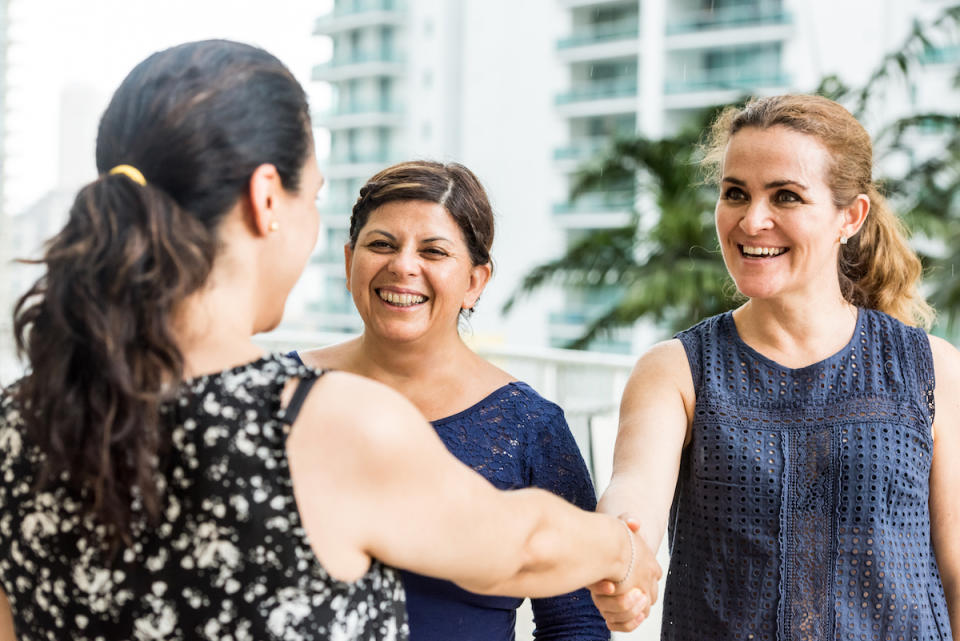 Three women outside with one shaking the other's hand