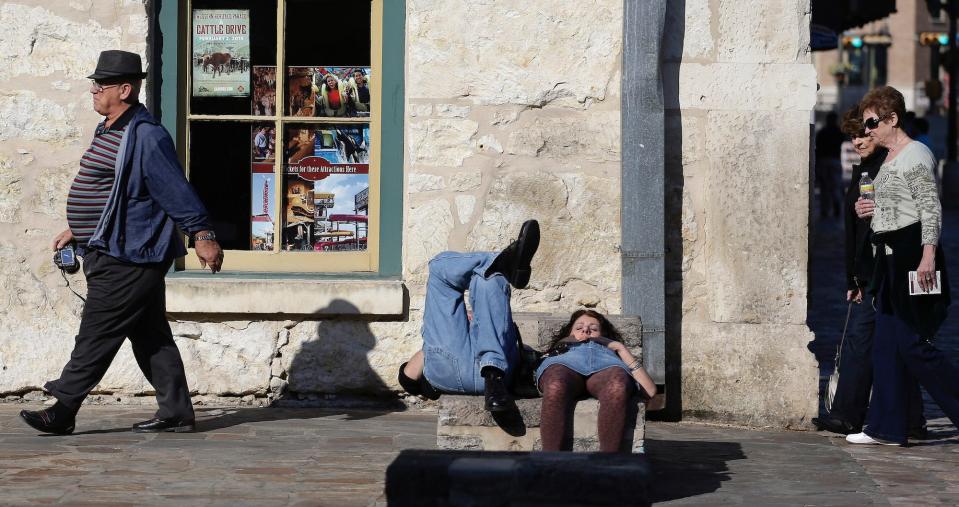 A couple nap in the sun as tourists pass by at Alamo Plaza in downtown San Antonio.