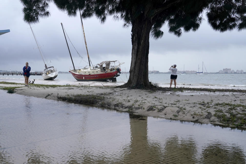 People walk past past boats on the beach in the aftermath of Tropical Storm Eta, Thursday, Nov. 12, 2020, in Gulfport, Fla. Eta dumped torrents of blustery rain on Florida's west coast as it slogged over the state before making landfall near Cedar Key, Fla. (AP Photo/Lynne Sladky)