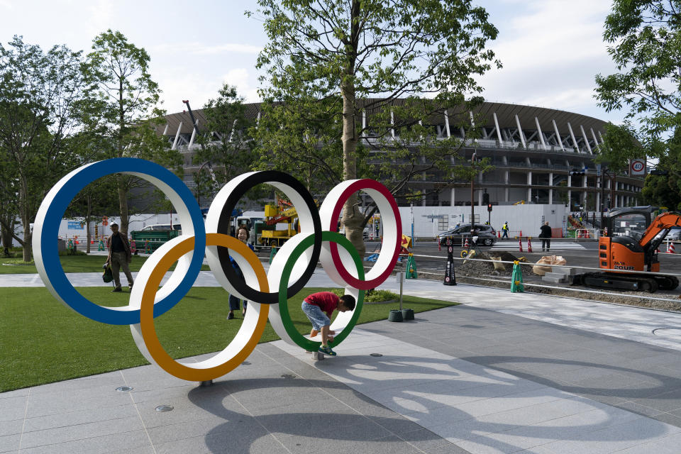 A boy walks through the Olympics rings while posing for photos as New National Stadium is seen in the background Monday, June 17, 2019, in Tokyo. The stadium will host the opening and closing ceremonies at the Tokyo 2020 Olympics. (AP Photo/Jae C. Hong)