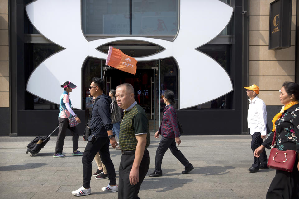 A Chinese tour guide leads a tour group past a store from American sportswear retailer Under Armour at an outdoor shopping area in Beijing, Tuesday, Sept. 25, 2018. A Chinese trade envoy said Tuesday that talks with Washington are impossible while the United States "holds a knife" to Beijing's neck by imposing tariff hikes. (AP Photo/Mark Schiefelbein)