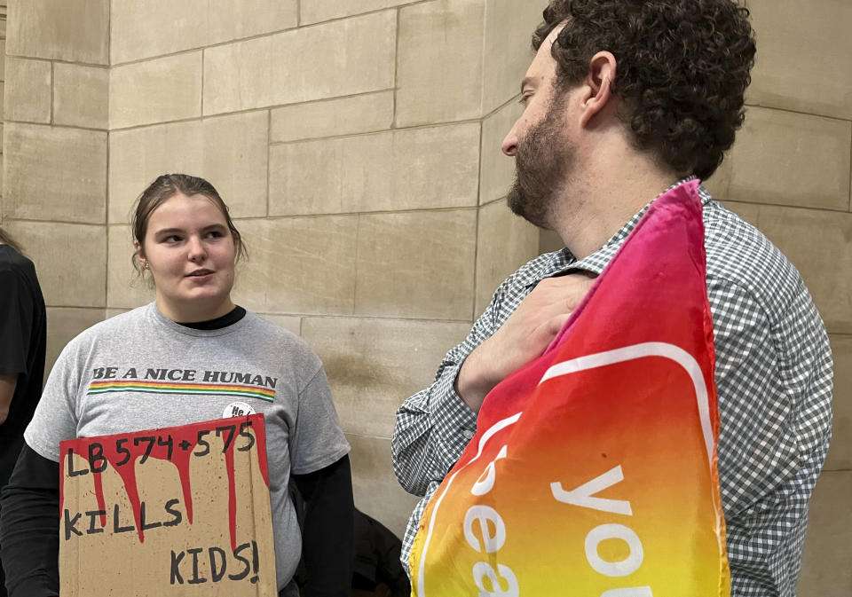 Elliott Braatz, 17, stands with Adam Downs, 41, in the Nebraska Capitol rotunda to protest a bill that would ban gender-affirming care for anyone 18 and younger in the state on Thursday, March 23, 2023. The contentious bill advanced Thursday, despite a threat by several lawmakers to filibuster the rest of the session if it moved forward. (AP Photo/Margery Beck)