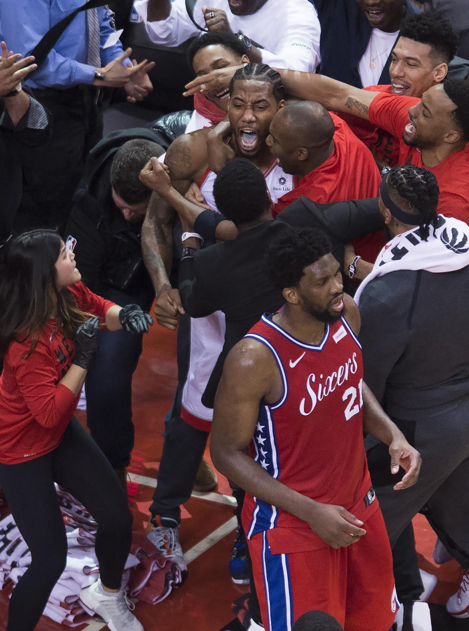 Toronto Raptors forward Kawhi Leonard, center, reacts with teammates after making the game-winning shot as Philadelphia 76ers center Joel Embiid (21) walks away at the end of an NBA Eastern Conference semifinal basketball game, in Toronto, Sunday, May 12, 2019. (Nathan Denette/The Canadian Press via AP)