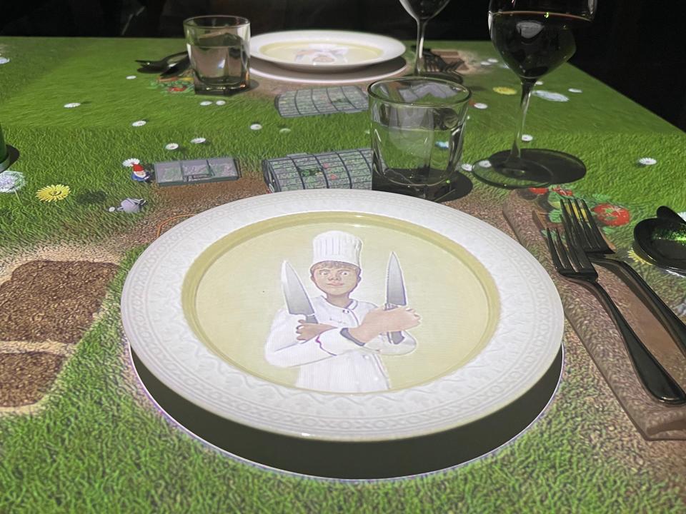 White plate with projected chef on it on green farmscape table at Le Petit Chef