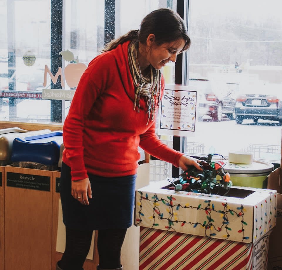 Woman in red sweater recycles Christmas lights at Mom's Organic Market.