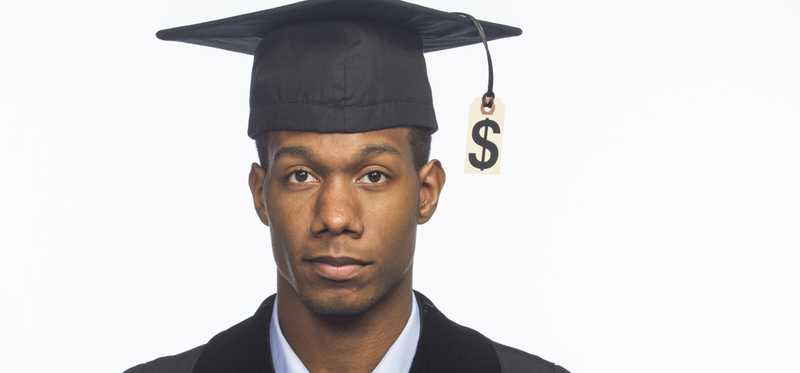 A young man in a graduation cap and gown, with a dollar sign hanging as the tassel on the cap.