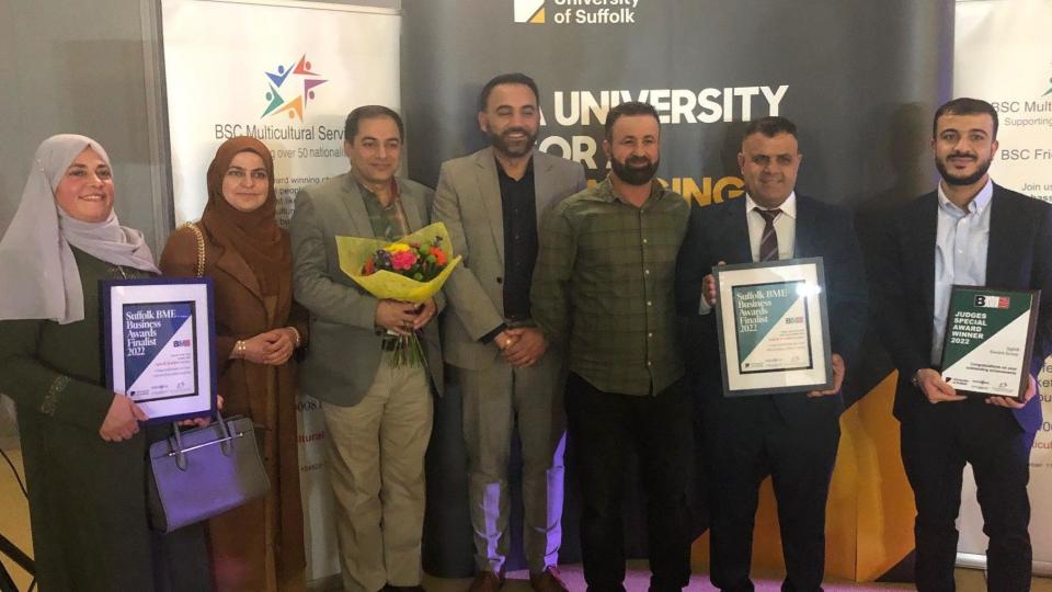 Seven people stand with certificates and flowers at an awards presentation