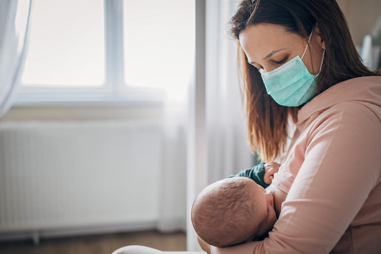 Two people, mother with protective mask breastfeeding her baby son at home, they are at home do to pandemic outbreak quarantine.