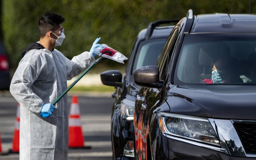 RIVERSIDE, CA - DECEMBER 21, 2021: A health care worker hands out a COVID-19 test kit at a Curative drive through testing site at La Sierra Park December 21, 2021 in Riverside, California.The Omicron variant is on the rise in Southern California and has a higher chance of infecting the unvaccinated.(Gina Ferazzi / Los Angeles Times)