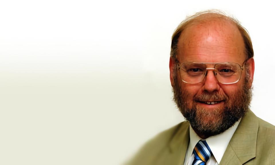 Portrait of Sir Ian Wilmut, the cloner of Dolly the sheep. The bearded man with glasses smiles for the camera over an off-white background.