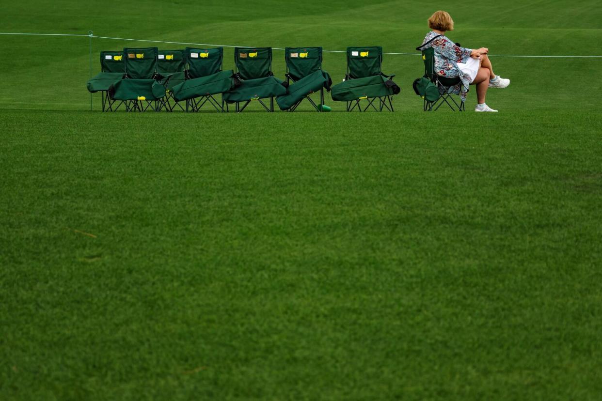 A patron looks on as they sit amongst empty chairs during the first round of the 2023 Masters.