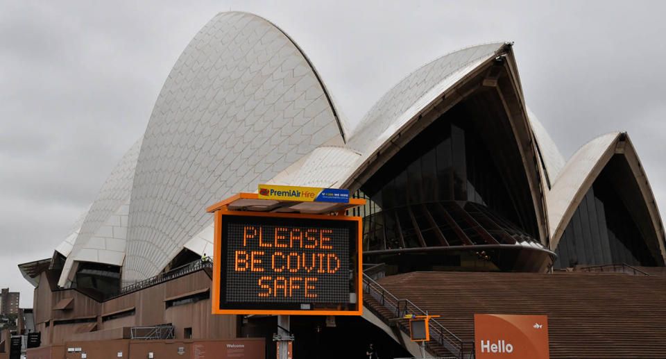 The Sydney Opera House with a Covid warning sign out the front asking people to be Covid safe.