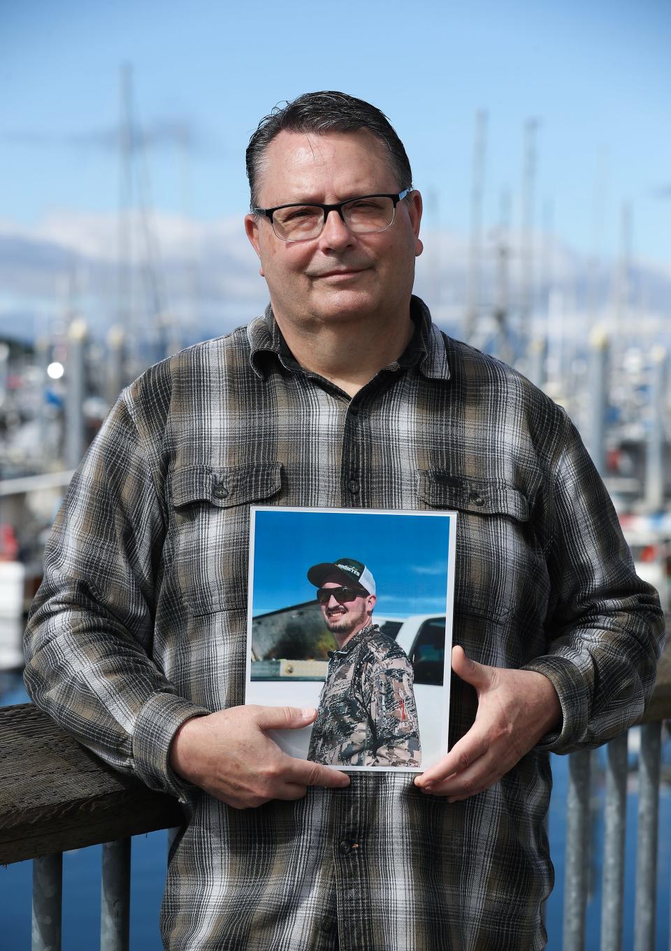 Gary Johnston stands near the harbor in Sitka, Alaska, on Aug. 26, 2023 while holding a photo of his son, Gabe Johnston, who died of a drug overdose. Denise Damewood has provided rescue kits to fishing boat captains to give to their crew in case of an overdose.