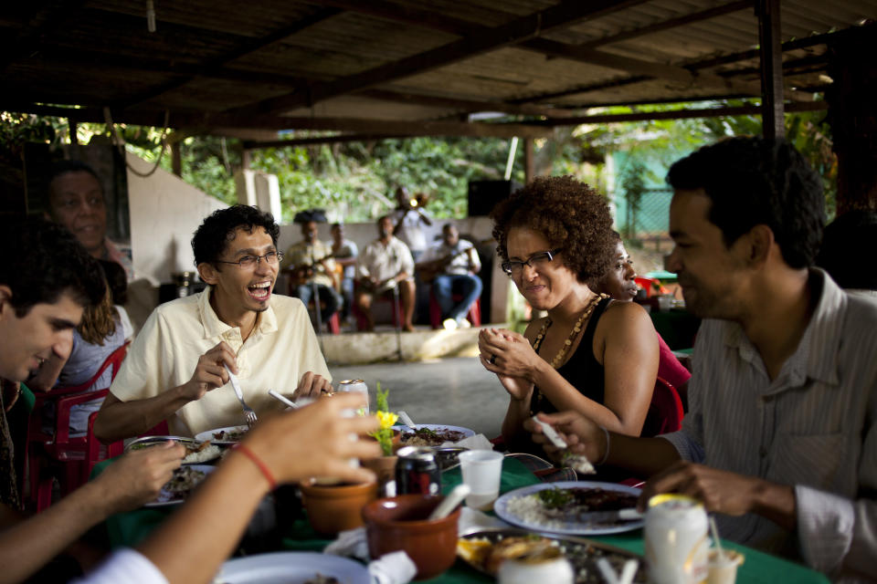 In this Sept. 15, 2012 photo, people enjoy a traditional stew called "feijoada" at the Quilombo Sacopa in Rio de Janeiro, Brazil. Quilombos are communities founded by escaped slaves or their descendents, and in Sacopa, the community is trying to save the grouping of brick houses and shacks nestled in the lush foilage of Brazil’s coastal rainforest where families have made their home for more than century but never legally owned. (AP Photo/Victor R. Caivano)