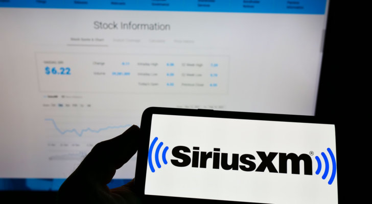 Person holding mobile phone with logo of US broadcasting company Sirius XM Holdings Inc. (SIRI) on screen in front of web page. Focus on phone display. Unmodified photo.