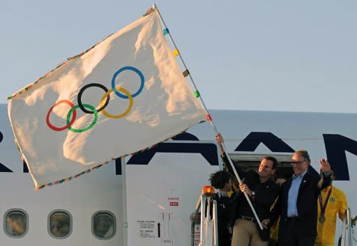 El alcalde de Rio de Janeiro, Eduardo Paes (I), ondea la bandera olímpica a su llegada de Londres junto a la delegación brasileña, este lunes. La bandera olímpica aterrizó este lunes en Rio de Janeiro, otorgando oficialmente a la ciudad el título de anfitriona de los Juegos Olímpicos de 2016 y los gigantescos desafíos que el honor conlleva. (AFP | vanderlei almeida)