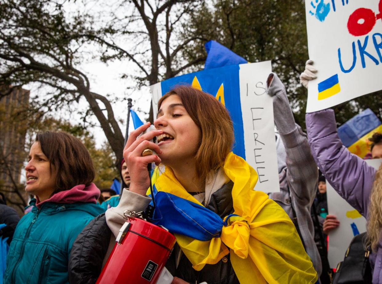 Ivanna Boychanko, draped in a Ukrainian flag, leads the crowd in song at the Capitol while protesting Russia's invasion of Ukraine on Thursday.