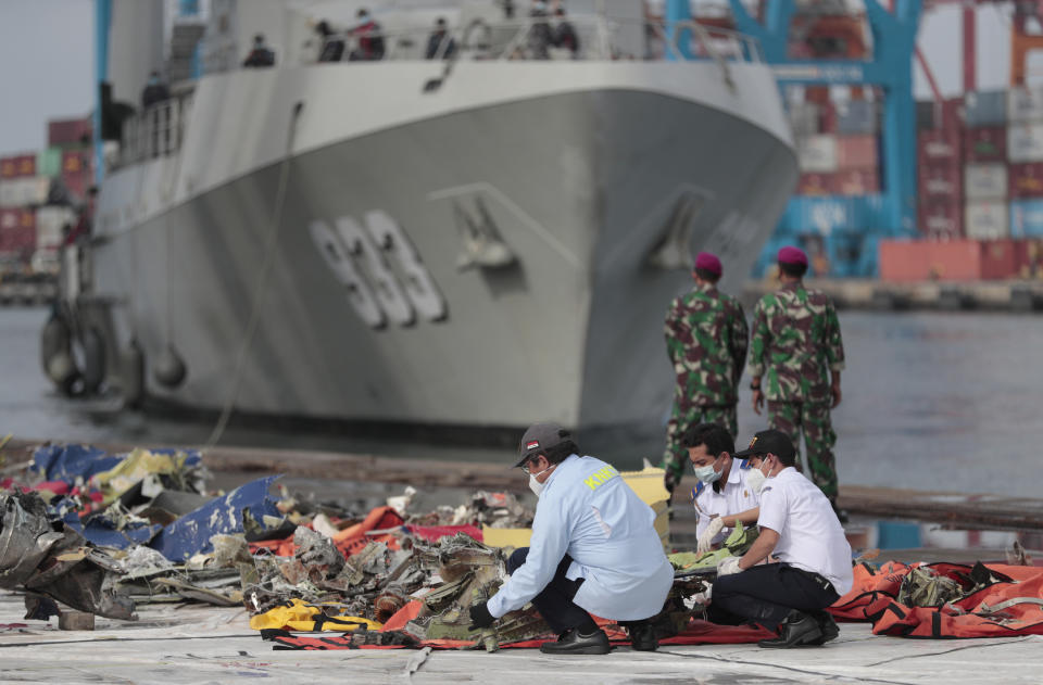 Investigators inspect pieces of the Sriwijaya Air flight SJ-182 retrieved from the Java Sea where the passenger jet crashed on Jan. 9, as an Indonesian Navy ship prepares to dock at Tanjung Priok Port in Jakarta, Indonesia, Thursday, Jan. 21, 2021. Indonesian authorities on Thursday ended the search for the wreckage of the plane that nose-dived into the sea, killing all of its passengers on board. (AP Photo/Dita Alangkara)