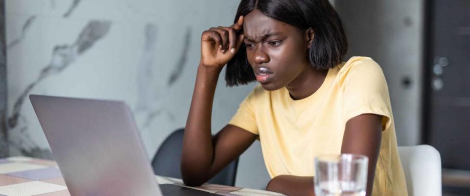 Upset african american woman sitting at kitchen table with laptop, dealing with financial stress and pressure because of mortgage debt, worrying a lot or feeling anxious over money