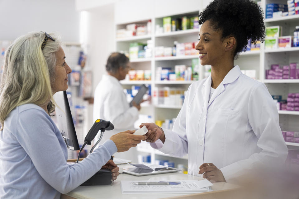 Mid-shot view of female African-American pharmacist handing prescription to customer while standing behind counter