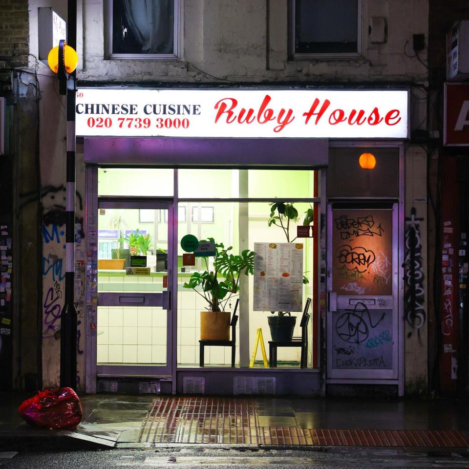 Ruby House Chhinese takeaway with plants on chairs in the window beside a door covered in graffiti