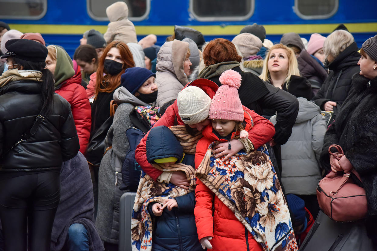 Refugees on a platform of a railway station, some wearing masks, embrace one another.
