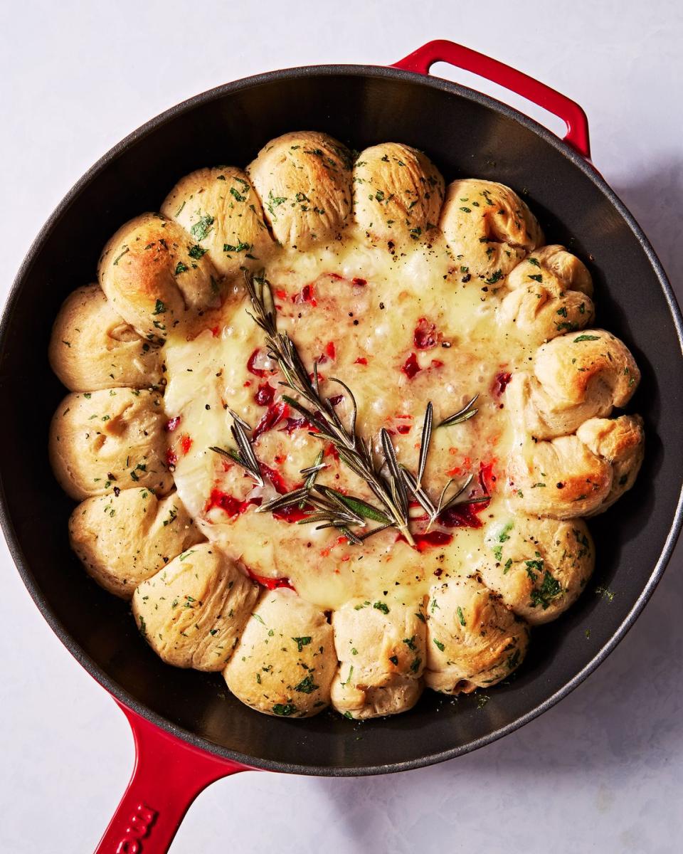 brie dip in a cast iron skillet swirled with cranberry sauce and surrounded by herby biscuits