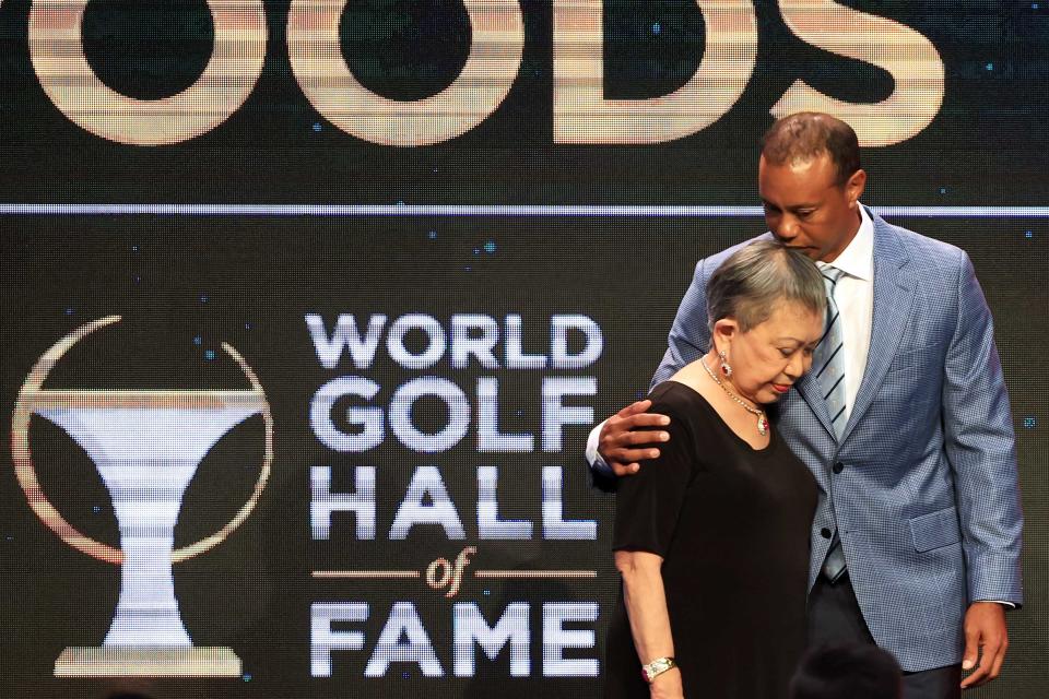 Tiger woods kisses the top of his mom's head as they stand in front of a black and gold screen. (Sam Greenwood / Getty Images)