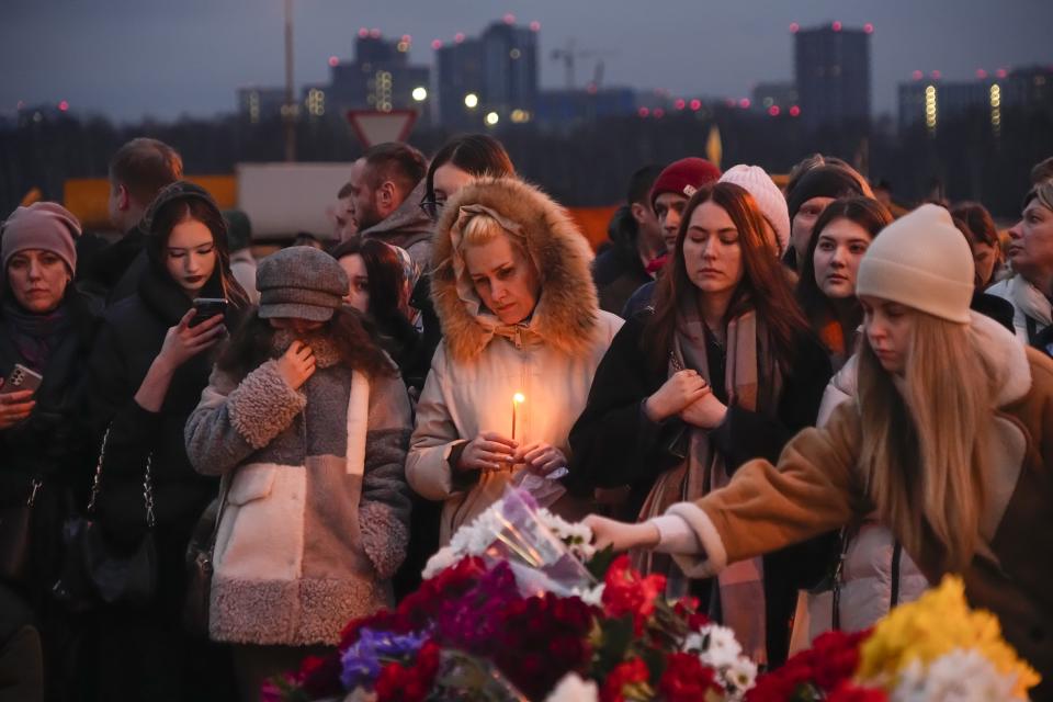 People lay flowers and light candles standing next to the Crocus City Hall, on the western edge of Moscow, Russia, Saturday, March 23, 2024. Russia's top state investigative agency says the death toll in the Moscow concert hall attack has risen to over 133. The attack Friday on Crocus City Hall, a sprawling mall and concert venue on Moscow's western edge, also left many wounded and left the building a smoldering ruin. (AP Photo/Alexander Zemlianichenko)