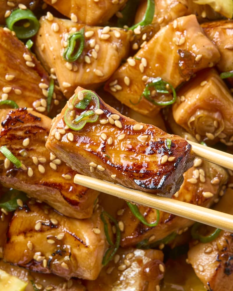 close up of a salmon bite being held up with chopsticks over the bowl of salmon.