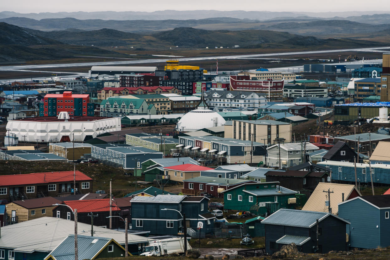 Dozens of tightly packed buildings of various shapes and sizes and colors in front of a low mountain range.