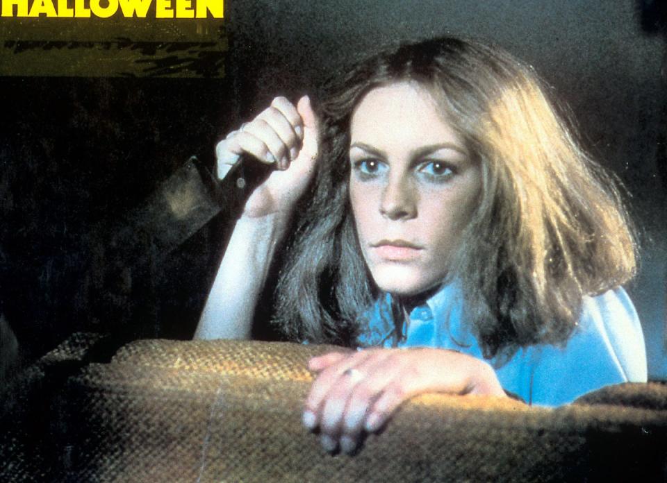 a photo of jamie lee curtis starring in the film halloween, holding a knife and looking over a couch