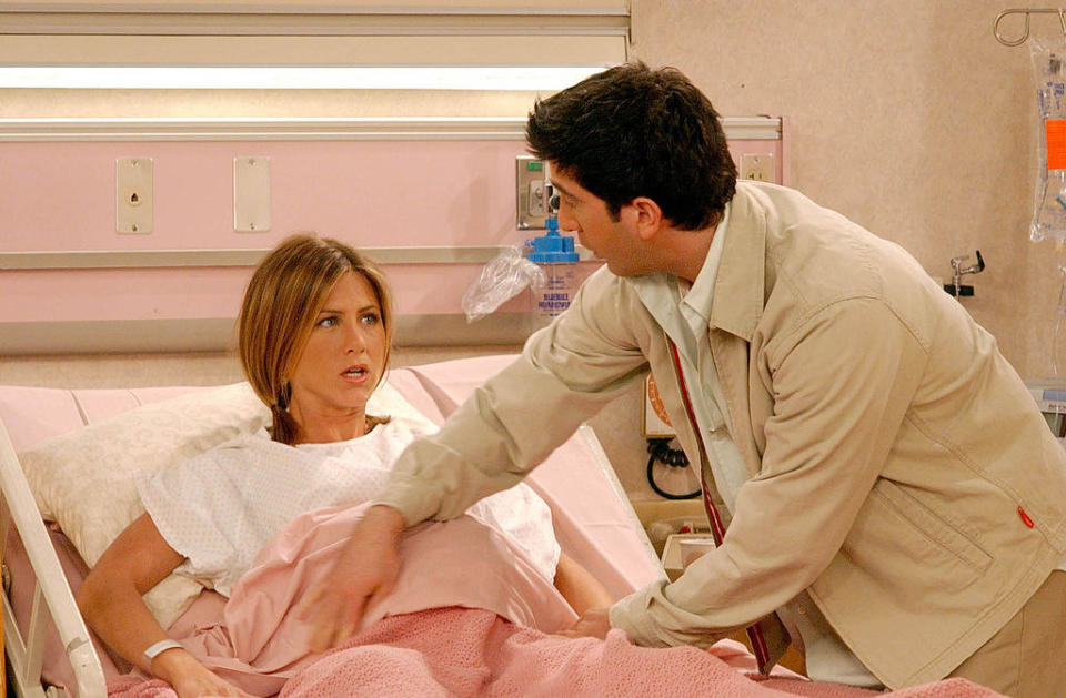 Rachel laying in the hospital bed whole Ross comforts her