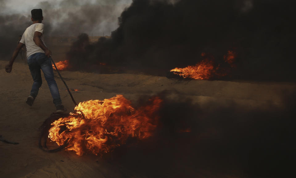 A protester pulls burning tire near the fence of the Gaza Strip border with Israel, during a protest east of Khan Younis, southern Gaza Strip, Friday, Oct. 5, 2018. Israeli forces shot dead three Palestinians, including a 13-year-old boy, as thousands of people protested Friday along the fence dividing the Gaza Strip and Israel, Gaza's Health Ministry said. (AP Photo/Adel Hana)