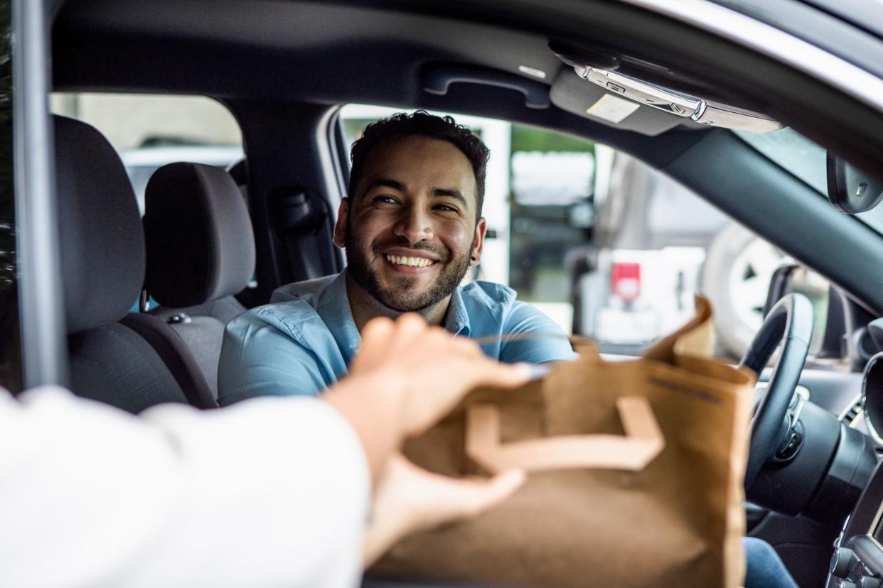 The mid adult man smiles when his curbside order is handed to him through the passenger window of his car.