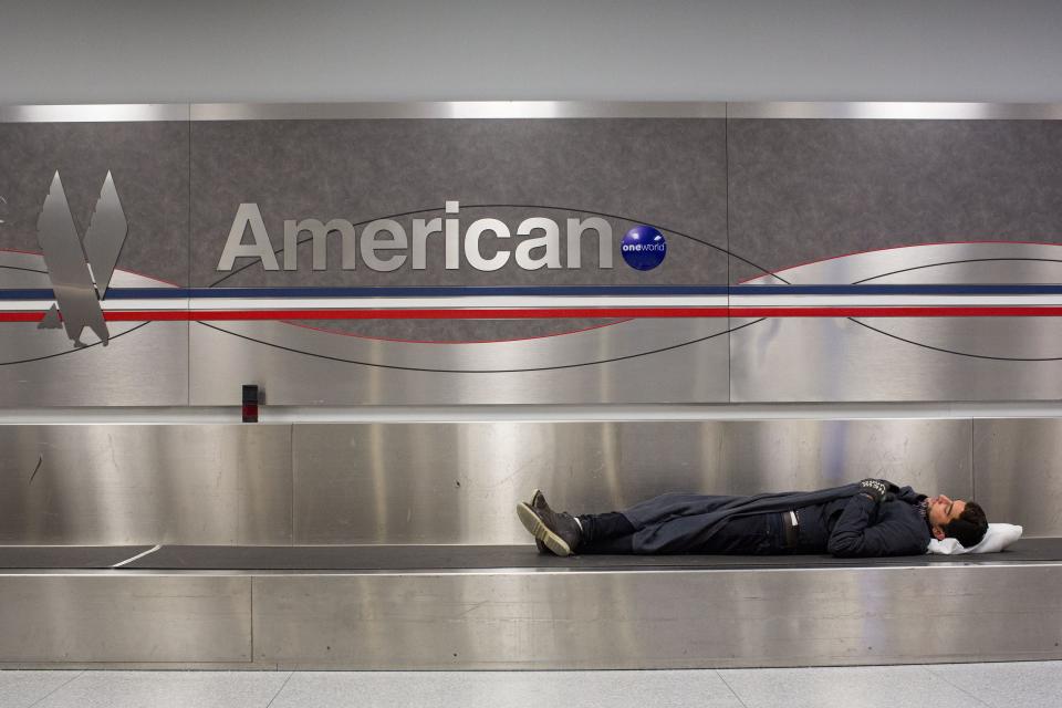 A man sleeps on a conveyer belt under an American Airlines logo at John F. Kennedy International Airport in New York