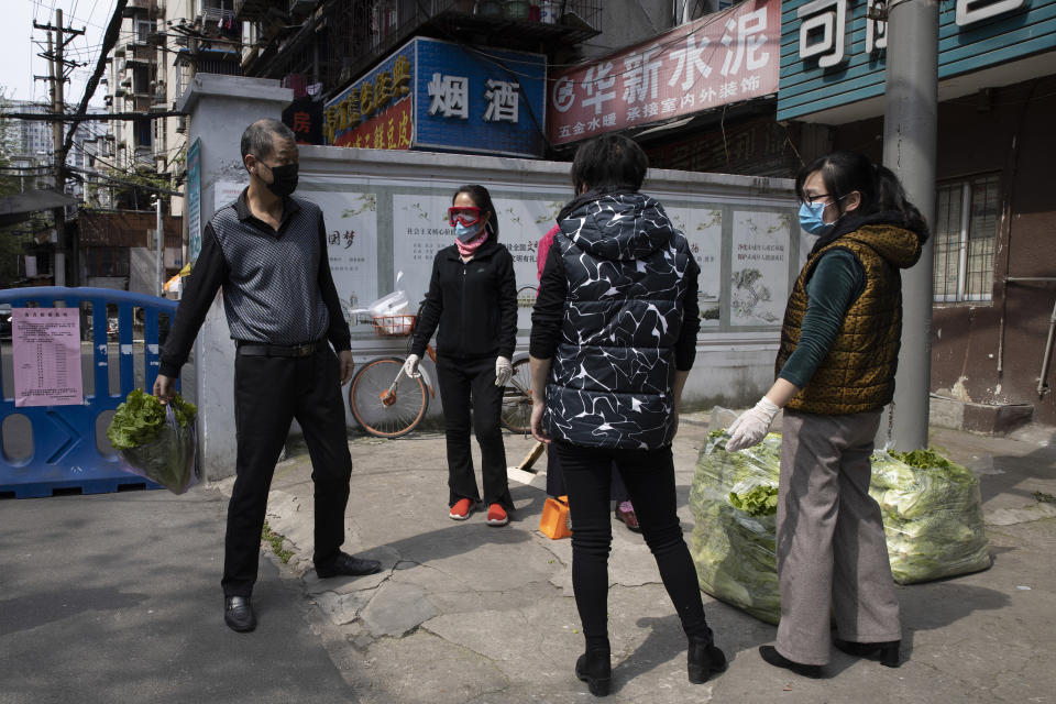 In this Monday, April 6, 2020, photo, a resident, left, collects his vegetable from volunteer residents outside a community in Wuhan in central China's Hubei province. Some farmers are finding temporary outlets for sales through volunteers in Wuhan helping the elderly and other vulnerable people get food supplies. They buy direct from farmers and arrange delivery to apartment complexes. (AP Photo/Ng Han Guan)