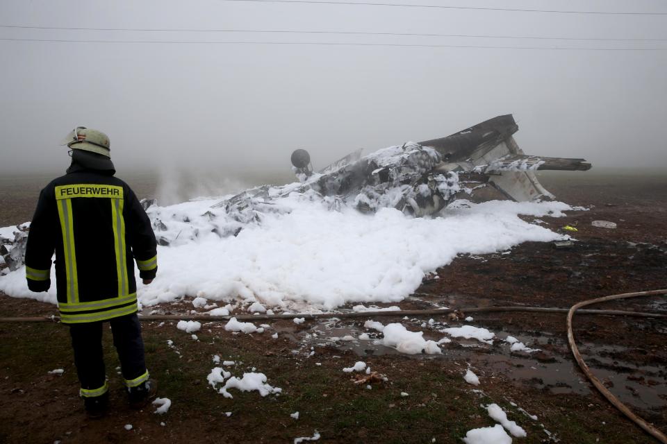 A firefighter stands next to the burnt-out wreckage of a twin-engine business jet near Foehren Germany, Sunday Jan . 12, 2014. Police say a small jet has crashed near an airfield in western Germany and four people on board are believed to have died. The plane came down Sunday lunchtime at a landfill site near the city of Trier. City police said in a statement that it appears to have been a Cessna Citation business jet carrying two pilots and two passengers from England to an airfield at Foehren, near the crash site. (AP Photo/dpa,Thomas Frey)