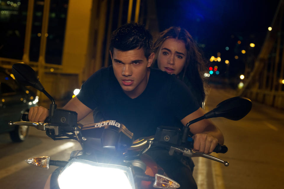 taylor driving a motorcycle with someone grabbing on to him