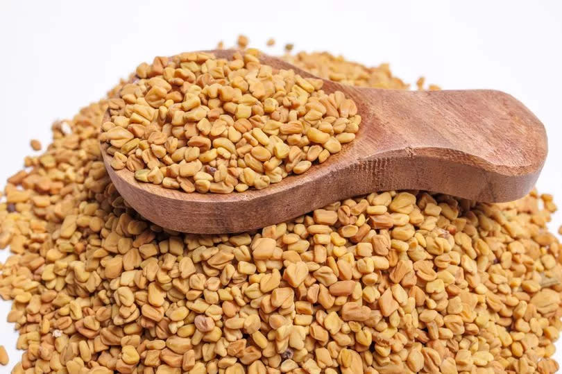 Close-up of fenugreek seeds piled with a wooden spoon resting on top isolated on White.