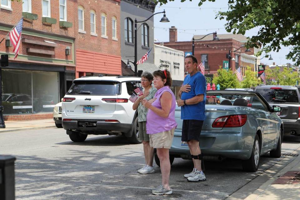 People wave flags and hold hands over their hearts on Monday afternoon as a hearse drives down East Main Street in Belleville carrying the casket of former Mayor Mark Eckert.