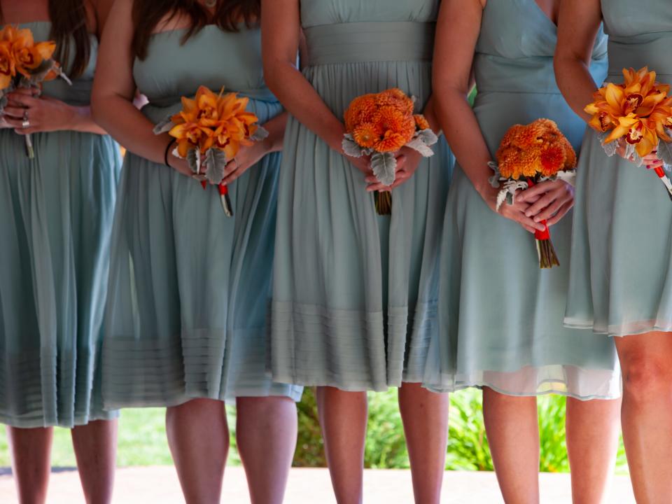 six bridesmaid standing in matching blue dresses holding orange bouquets