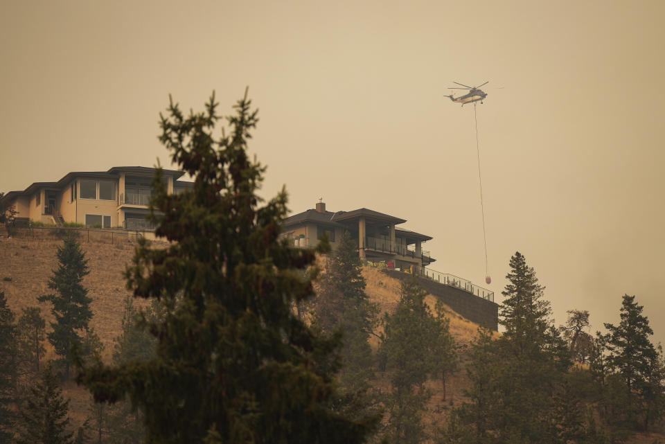 A helicopter with a water bucket flies past homes in the Wilden neighbourhood near Knox Mountain after RCMP officers enforced a new wildfire evacuation order in Kelowna, British Columbia, Friday, Aug. 18, 2023. (Darryl Dyck/The Canadian Press via AP)