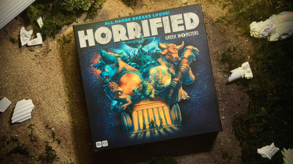 The box of Horrified: Greek Monsters on a sandy floor with broken Greek pillars surrounding it