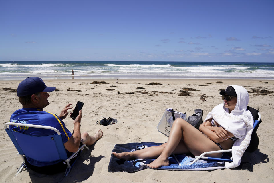 Ken, left, and Ana Seastrom wear no masks as they sit on the beach Tuesday, April 27, 2021, in San Diego. Ken is fully vaccinated and Ana has already had one shot of vaccine. U.S. health officials say fully vaccinated Americans don't need to wear masks outdoors anymore unless they are in a big crowd of strangers. And unvaccinated people can drop face coverings in some cases, too. (AP Photo/Gregory Bull)