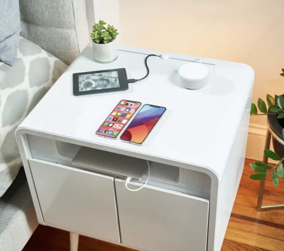 A white end table with devices charging on it